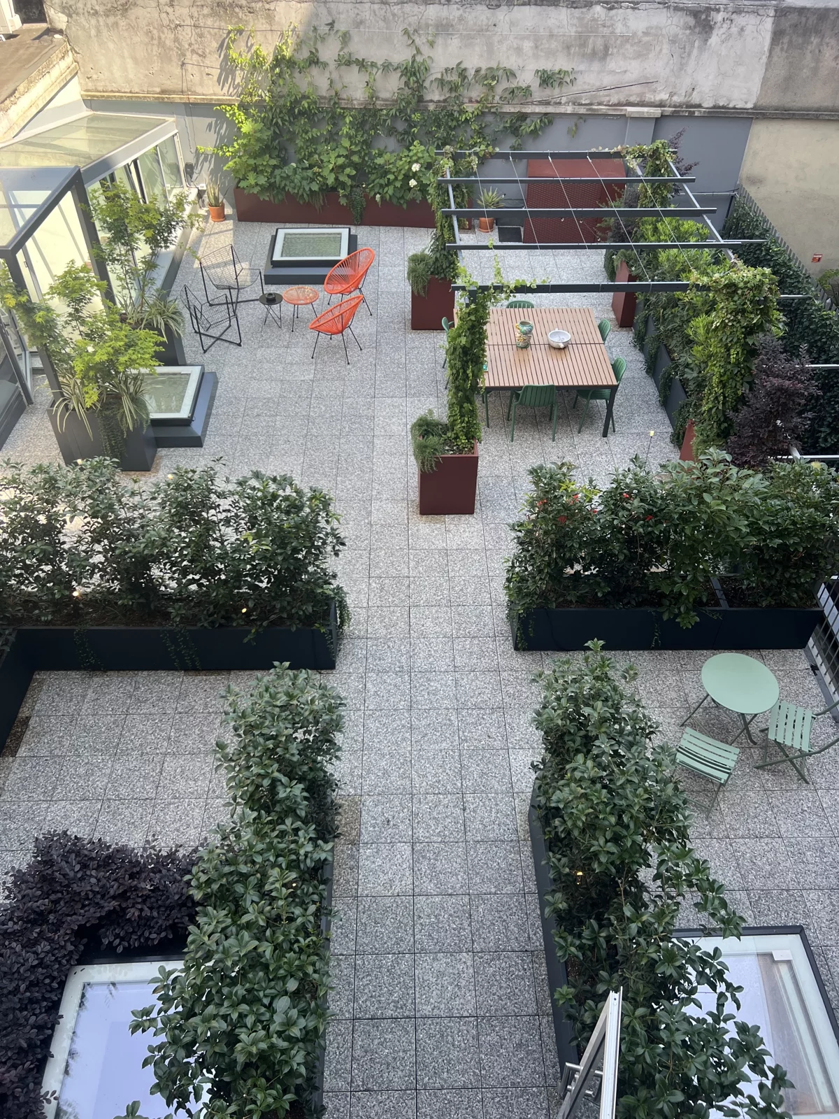 Grande terrazzo visto dall'alto: fioriere basse, pergola con tavolo da pranzo e sedute tra il verde